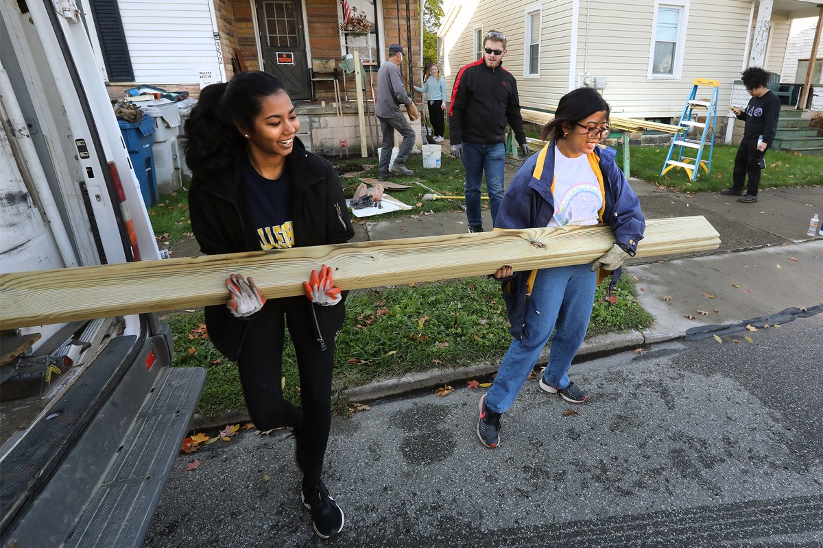 Two girls carrying a piece of lumber.